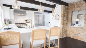 Une cuisine moderne avec des armoires blanches, un grand îlot central et des chaises en bois. On y trouve un mur en pierre et une fenêtre offrant une belle vue.