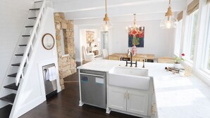 Une cuisine moderne dotée d’un îlot central, de meubles blancs et d’un mur d’accent en pierre.