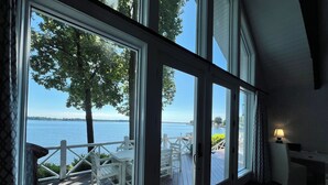 Une pièce dotée de grandes fenêtres donnant sur un lac, une terrasse en bois avec des meubles d’extérieur et une vue sur l’eau.