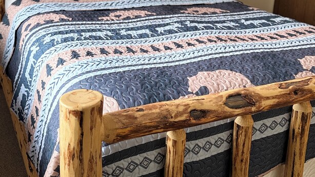 Una cama con estructura de madera, colcha estampada y dos almohadas con motivos de animales.