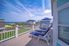 A deck with lounge chairs and a view of the beach and ocean.