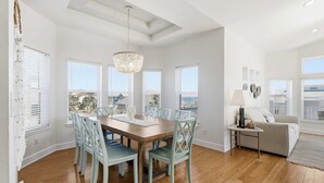 A dining area with a wooden table, light blue chairs, and a chandelier. - Beachfront 5BR | Ocean Views, Elevator & Game Room (Palm Coast)