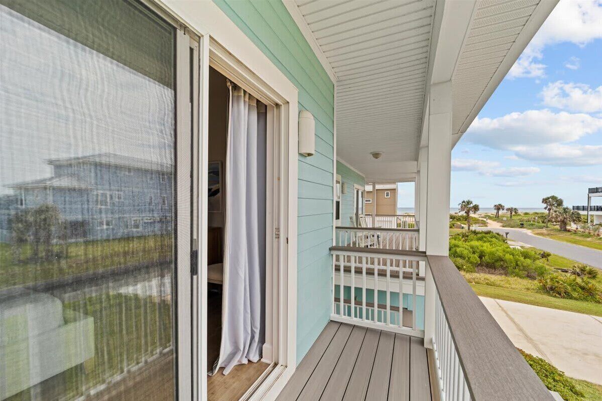 A balcony with a view of the beach, a sliding glass door, and a white railing.