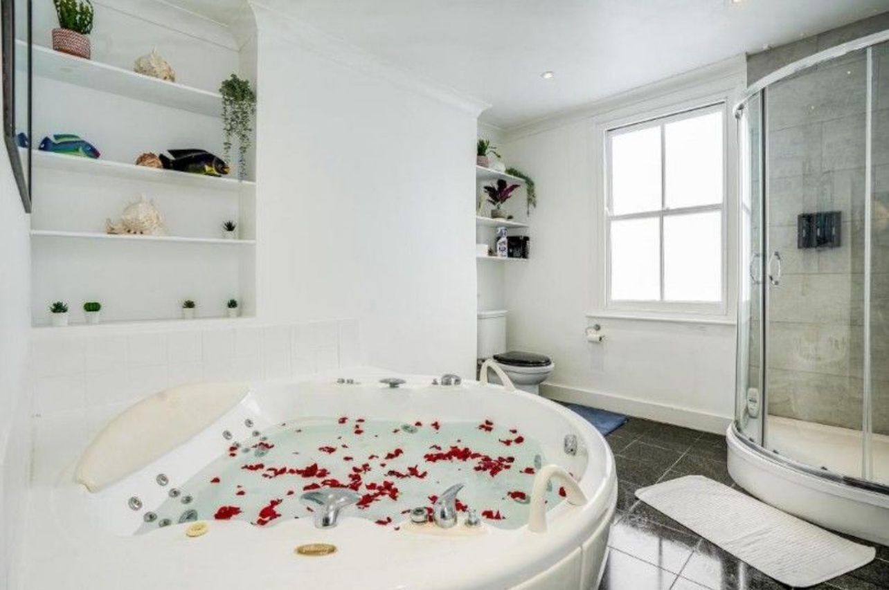 A modern bathroom with a bathtub filled with rose petals, a glass shower enclosure, and shelves with decorative items.