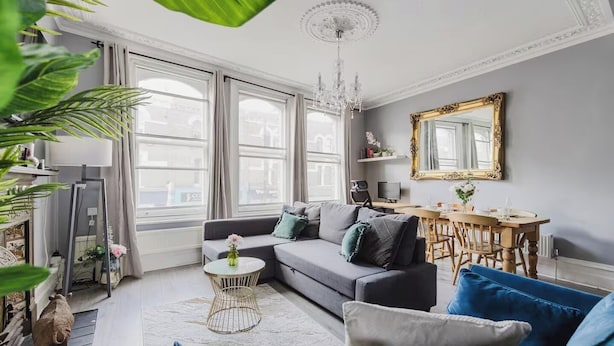 A modern living room with a sofa, coffee table, and blue chairs. There is a dining table with chairs and a chandelier. - Elegant 3 Bedroom Fulham-Chelsea Home/ Rooftop Terrace/ Jacuzzi/ Sleeps 8 (London)