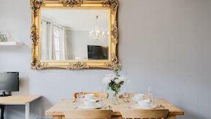 A dining area with a large ornate mirror, a wooden table set for two, and a television on a side table. - Elegant 3 Bedroom Fulham-Chelsea Home/ Rooftop Terrace/ Jacuzzi/ Sleeps 8 (London)