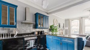 A modern kitchen with blue cabinets, a black and white checkered floor, and a large window providing natural light. - Elegant 3 Bedroom Fulham-Chelsea Home/ Rooftop Terrace/ Jacuzzi/ Sleeps 8 (London)