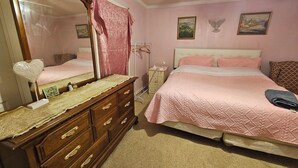 A bedroom with a large mirror, a dresser, a bed with pink bedding, and two paintings on the wall. - 3-bedroom house in delightful S Raleigh WiFi, AC (Raleigh)