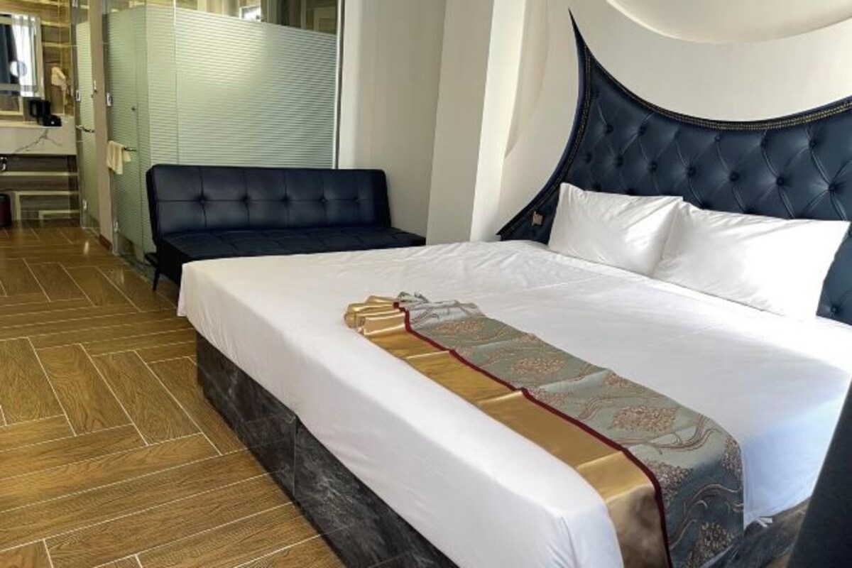 A hotel room with a large bed, a dark headboard, and a wooden floor.