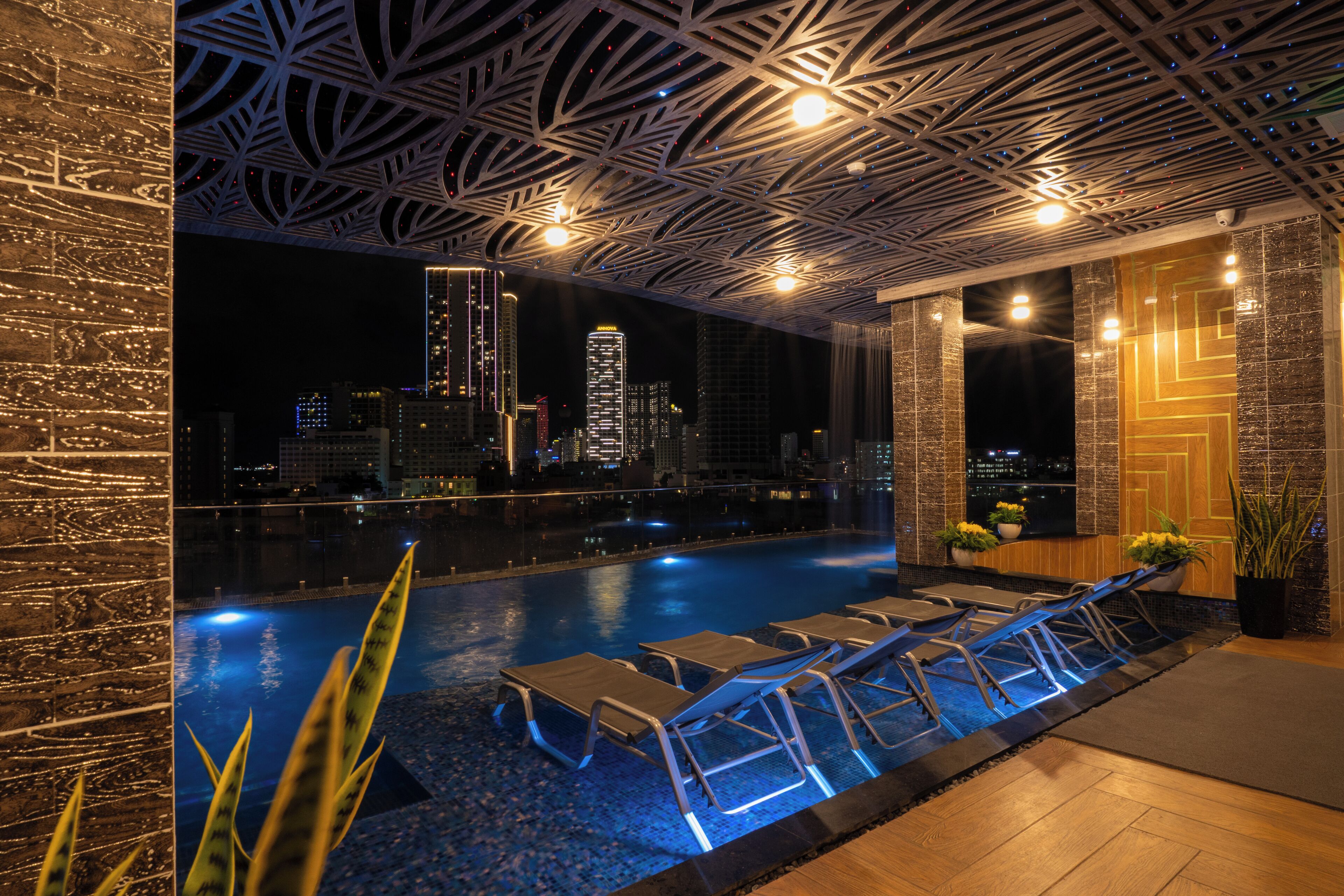 A rooftop pool with lounge chairs and a cityscape view at night.