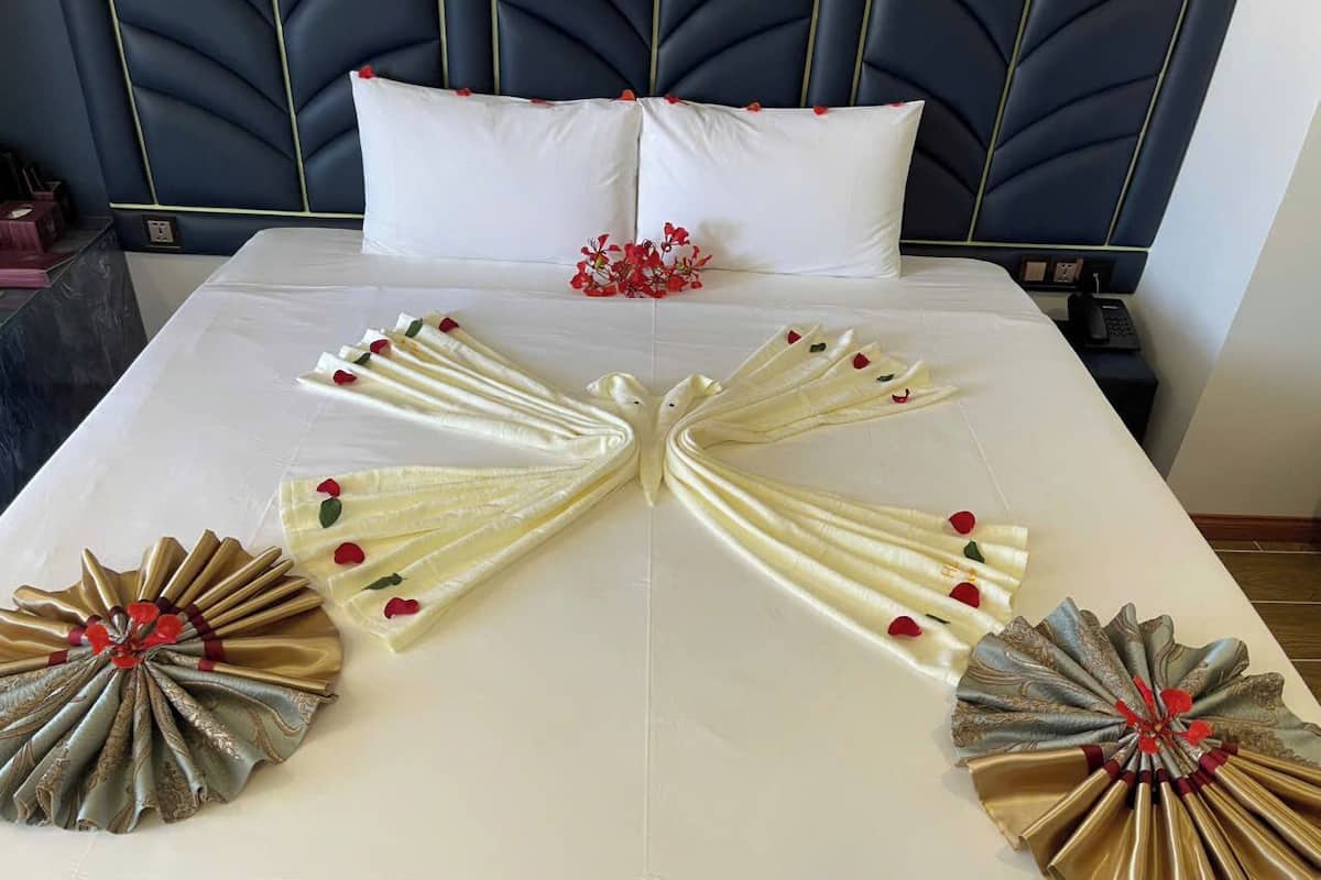 A neatly made bed with decorative pillows and a unique fan-shaped arrangement of white and gold fabric.