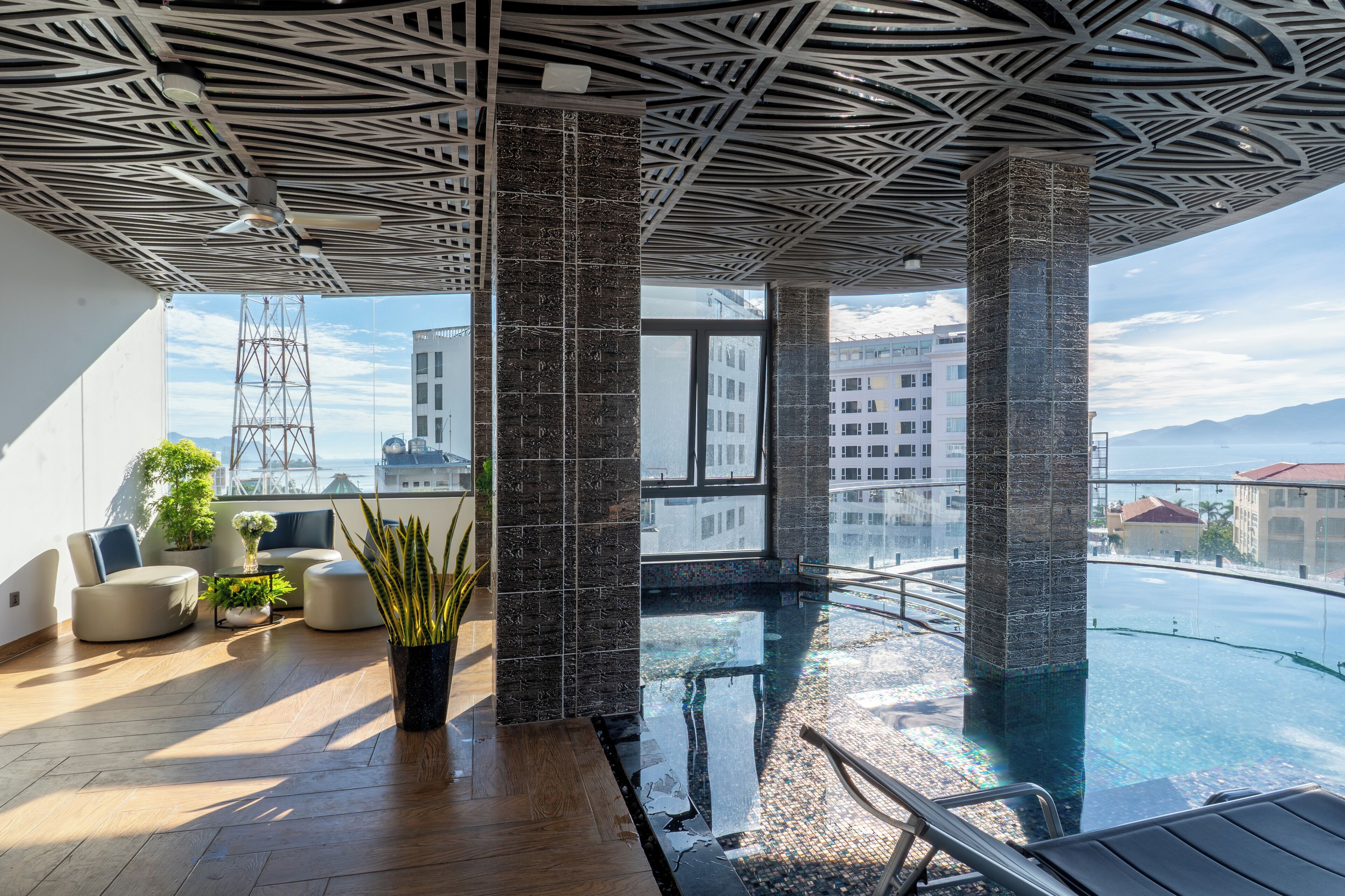 A modern indoor pool area with a ceiling design, seating, and a view of the cityscape.