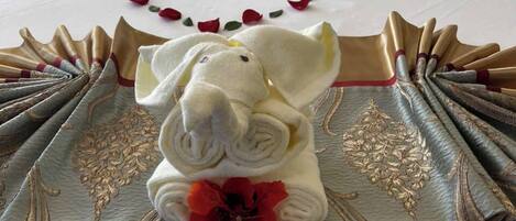 A bed with a decorative towel arrangement featuring swans and an elephant, a red rose, and a gold-patterned cloth.