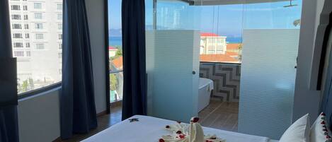 A hotel room with a large bed, a view of the city, and a balcony with a table and chairs.
