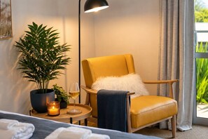 A room with a yellow armchair, a potted plant, a candle, and a glass of wine on a small table. - Lake View Lodge (Queenstown)