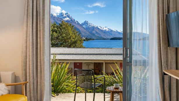 Une pièce avec vue sur les montagnes et un lac, un coin repas avec une table et des chaises, et une chaise jaune.