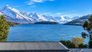 A lake with snow-capped mountains in the background, a clear sky, and a building with a sloped roof in the foreground. - Lake View Lodge (Queenstown)
