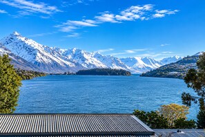 A lake with snow-capped mountains in the background, a clear sky, and a building with a sloped roof in the foreground.