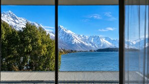 Une vue sur un lac, avec des montagnes enneigées en arrière-plan, une terrasse en bois et un bâtiment doté d’un toit en pente.
