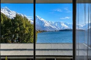 A view of a lake with snow-capped mountains in the background, a wooden deck, and a metal railing. - Lake View Lodge (Queenstown)