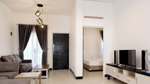 A modern living room with a sofa, coffee table, TV, speakers, and a door leading to another room. - Villa Normandie (Cimahi)