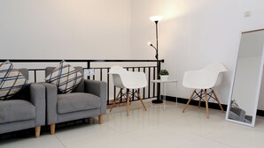 A modern living room with a grey sofa, white chairs, a small table, and a floor lamp. - Villa Normandie (Cimahi)