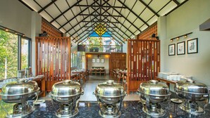 A buffet setup with multiple silver chafing dishes on a marble countertop, wooden partitions, and a high ceiling with a geometric pattern. - Vbrings Oak Village (Devikolam)