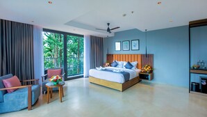 A modern hotel room with a large bed, a seating area with two chairs, a small table with flowers, and a balcony with curtains. - Vbrings Oak Village (Devikolam)
