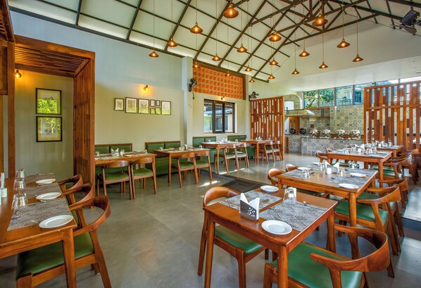 Un restaurante con mesas y sillas de madera, un techo alto con luces colgantes y vistas al exterior.