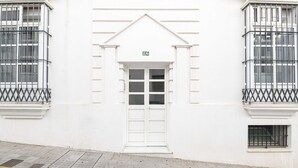 Een wit gebouw met een witte deur en ramen, nummer 26, met een klein balkon en een raam met een metalen traliewerk.