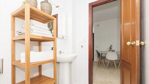 Een badkamer met een houten plank met handdoeken, een witte wastafel en een spiegel.