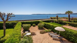 Ein gepflegter Garten mit Sitzgelegenheit, einer Palme und Meerblick.