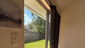 A room with a sliding glass door leading to a backyard with a wooden fence and a grassy lawn.