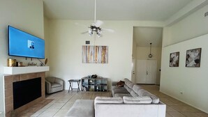 A living room with a grey sofa, a flat-screen TV, a fireplace, a ceiling fan, and artwork on the walls.