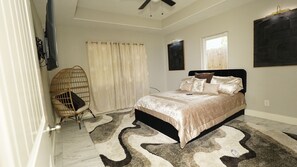 Relax in this serene bedroom with a large bed, a woven chair, and a ceiling fan.