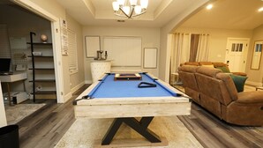 Une table de billard dans une pièce où se trouve un porte-queues, un canapé confortable et un bureau avec un globe terrestre et un calendrier.