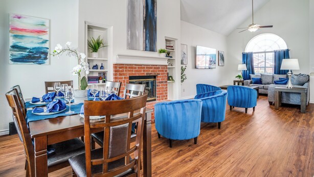 A spacious living room with a fireplace, wooden flooring, and blue upholstered chairs.