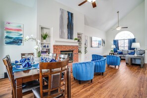 A spacious living room with a fireplace, wooden flooring, and blue upholstered chairs.
