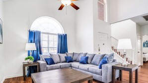 A living room with a sectional sofa, a coffee table, a ceiling fan, and a staircase leading to another level.