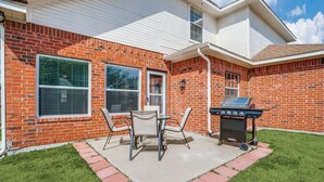 A backyard with a brick house, a grill, and a patio table with chairs.