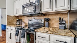 A kitchen with white cabinets, a stainless steel microwave, a stove, and granite countertops.