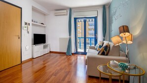 Una sala de estar moderna con un televisor de pantalla plana, un sofá, una mesa de centro de vidrio y una lámpara.