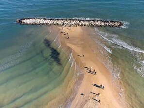 An aerial view of a beach with a rocky breakwater, clear water, and a few people.