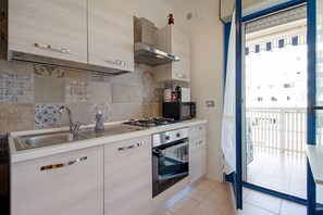 Une cuisine moderne équipée d’une cuisinière à gaz, d’un four et d’un évier intégrés, avec vue sur un balcon et un immeuble en arrière-plan.