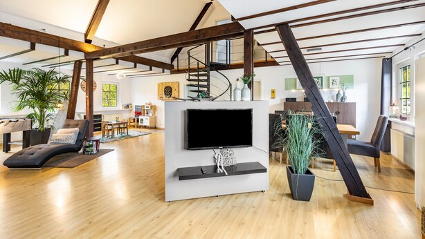 Amplia sala de estar con un mueble moderno para televisión, vigas de madera, una escalera y un comedor.