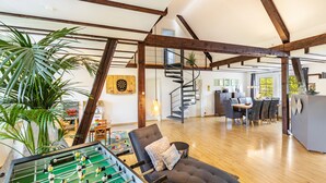 Un loft espacioso con vigas de madera a la vista, una mesa de fútbolín, una zona de comedor y una escalera que sube a un nivel superior.