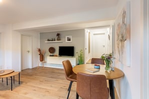 A modern living room with a dining area, a flat-screen TV, and a large abstract painting.