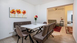 Un coin repas avec une table blanche, des chaises marron et un tableau représentant des fleurs accroché au mur.