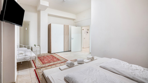 Une chambre d’hôtel moderne équipée d’un lit, d’une télévision, d’une armoire, d’un bureau et d’un tapis rouge à motifs.