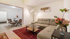 Un salon moderne avec un canapé, une table basse en verre, un coin repas avec des chaises, un tapis rouge à motifs et un vase de fleurs posé sur une table d’appoint.